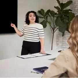 The image captures a professional setting where a woman is standing and presenting.