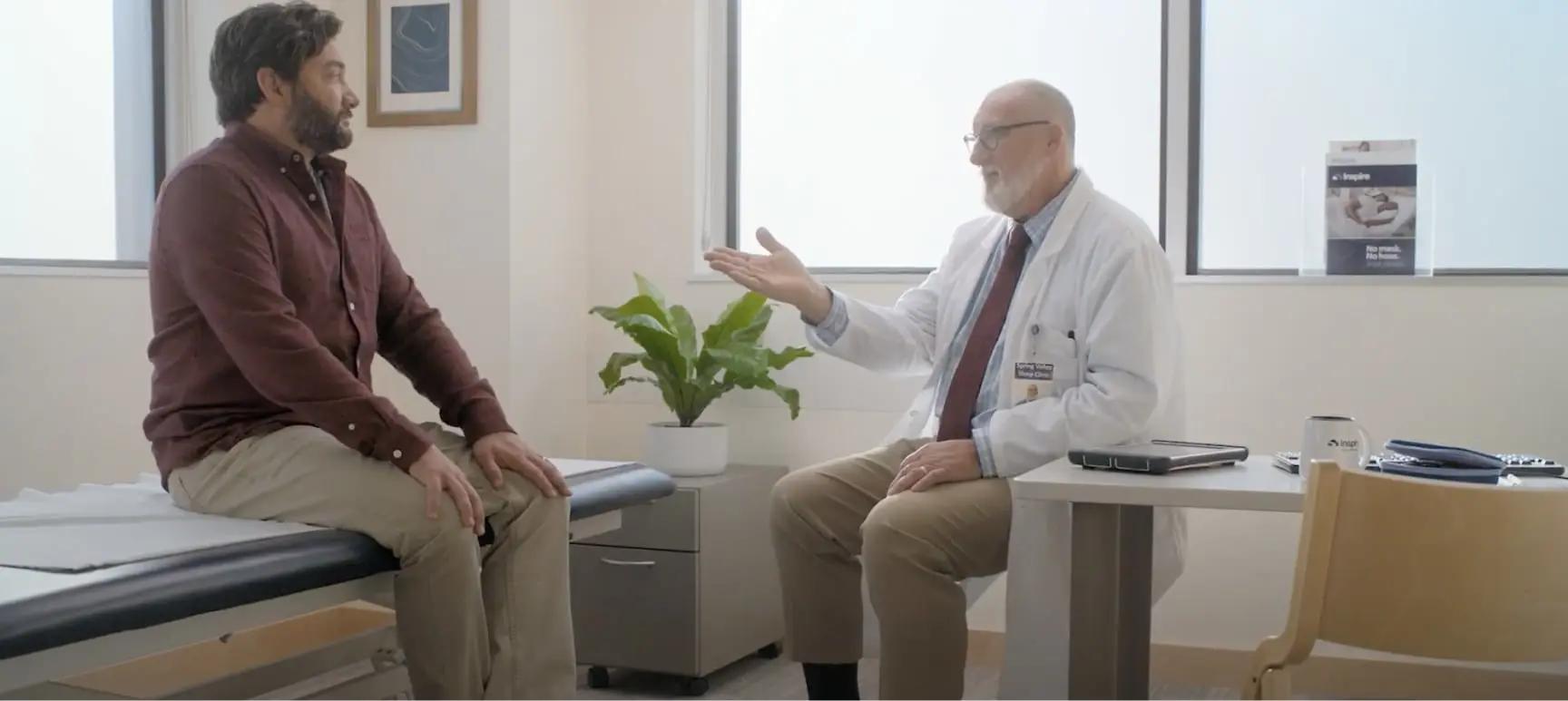 The image shows a conversation between a male patient and a male healthcare provider in a medical office.